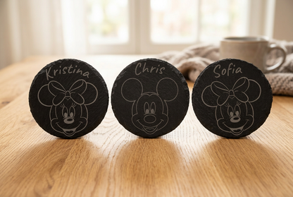 Three named engraved slate coasters on an oak table